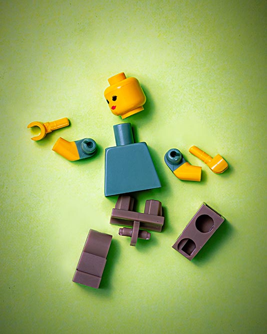 LEGO minifig broken into pieces against green background, photo by Jackson Simmer